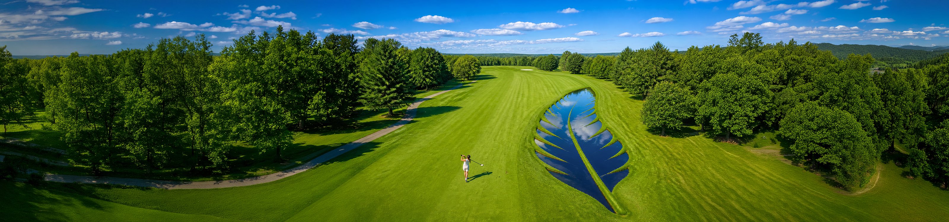 A golfer finishing her swing on a wide fairway, beside a pond shaped like a feather